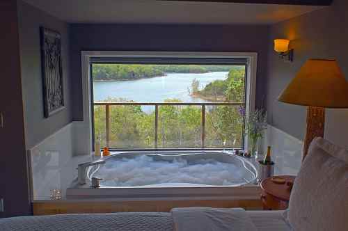A cozy bathroom with a jetted tub overlooking a scenic view of a river and lush greenery outside.