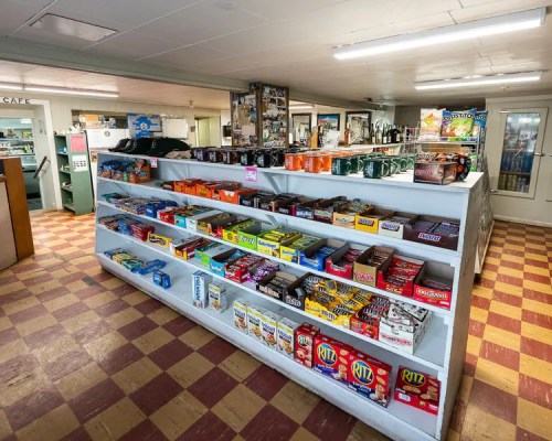 A display shelf filled with various snacks and candies in a small store with a checkered floor.
