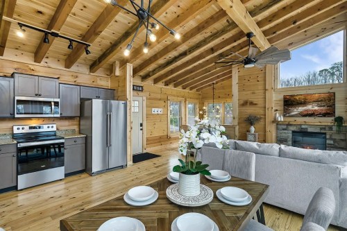 Cozy wooden cabin interior featuring a kitchen, dining area, and living space with a fireplace and large windows.
