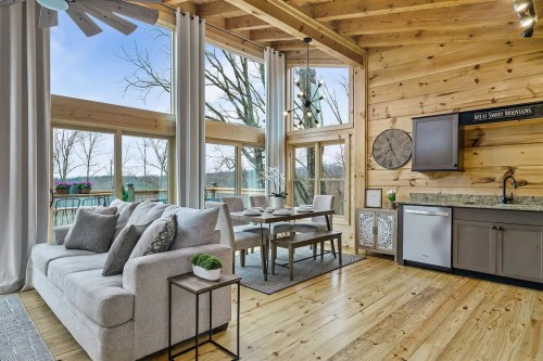 Cozy living area with wooden walls, large windows, a dining table, and a modern kitchen in a bright, airy space.