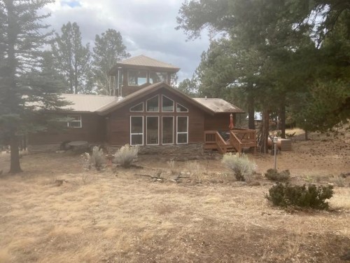 A wooden cabin surrounded by trees, featuring large windows and a deck, set in a dry, grassy landscape.