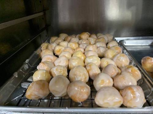 A tray filled with glazed doughnut holes, stacked closely together in a metal container.