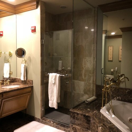 Luxurious bathroom featuring a glass shower, marble accents, a large mirror, and elegant fixtures.