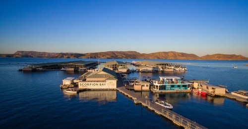 Aerial view of Scorpion Bay marina with boats and docks, surrounded by calm water and distant hills under a clear sky.