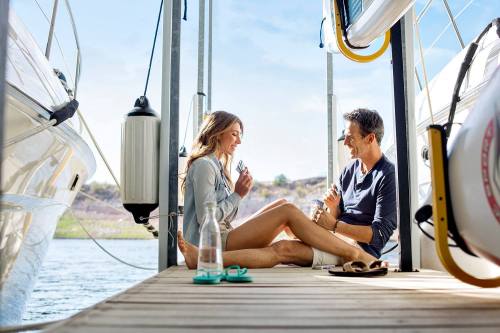 A couple sits on a dock by the water, enjoying each other's company and smiling, surrounded by boats.