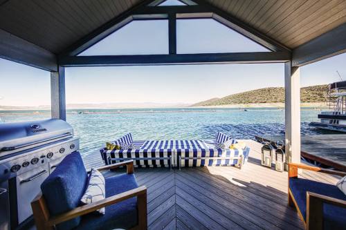 A cozy outdoor seating area with a striped couch and grill, overlooking a serene waterfront view.