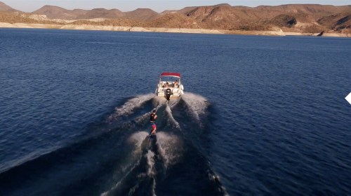 A person water skiing behind a boat on a calm lake, surrounded by mountains and clear blue skies.