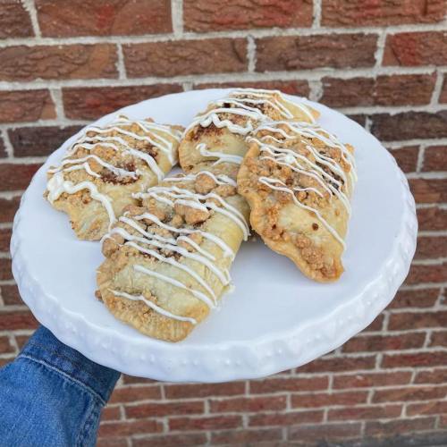 A plate of four drizzled pastries with a crumbly topping, held against a brick wall background.