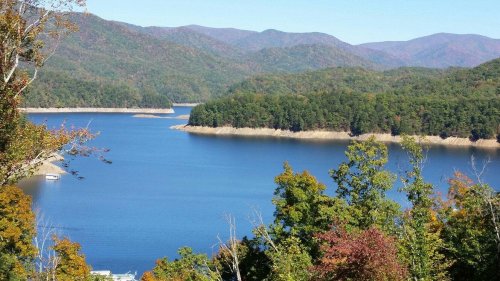 A serene lake surrounded by lush green trees and distant mountains under a clear blue sky.