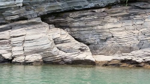 Layered rock formations beside calm green water, showcasing natural textures and colors.