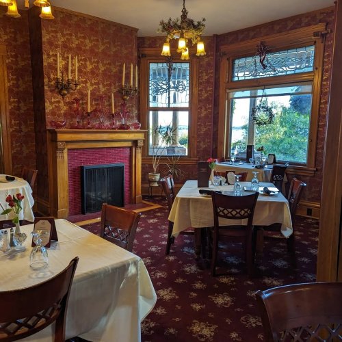 Cozy restaurant interior with elegant tables, a fireplace, and vintage decor featuring floral wallpaper and chandeliers.