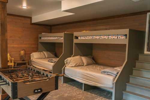 A cozy basement room with two bunk beds and a foosball table, featuring wooden walls and soft lighting.