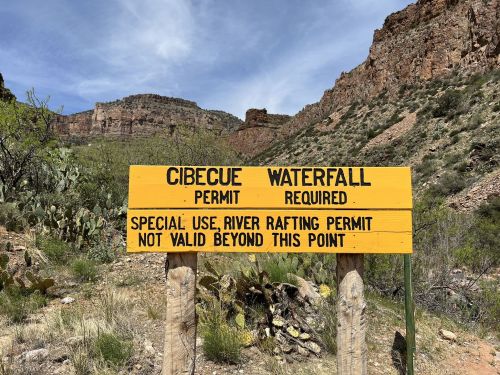 Sign for Cibecue Waterfall indicating permit requirements and river rafting permit restrictions. Scenic mountainous background.