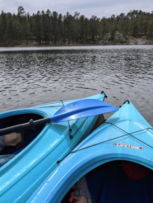Two blue kayaks on a calm lake, surrounded by trees and rocky terrain in the background.