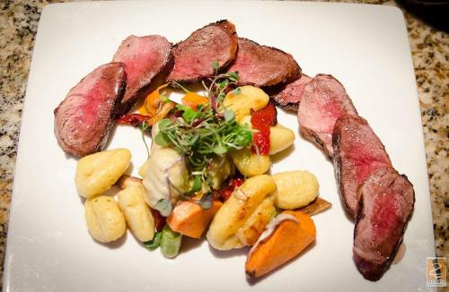 A plate featuring sliced cooked meat alongside a colorful vegetable and gnocchi salad, garnished with microgreens.