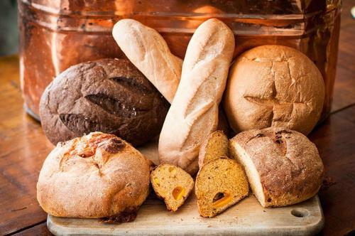 An assortment of freshly baked breads, including loaves, rolls, and sliced pieces, arranged on a wooden board.