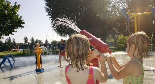 Children play in a splash pad, enjoying water sprays and sunshine on a warm day.