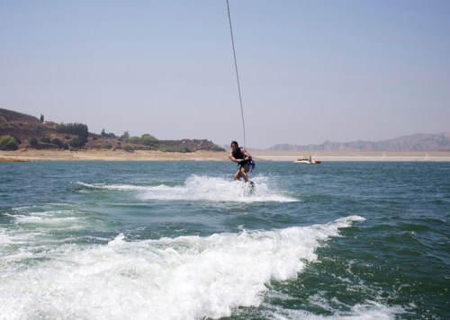 A person water skiing on a lake, creating splashes as they glide across the water under a clear blue sky.