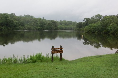 A calm lake surrounded by trees, with a sign stating "No fishing, swimming, or boats" in the foreground.