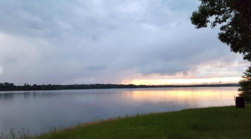 A tranquil lake at sunset, with cloudy skies and a hint of orange reflecting on the water's surface.