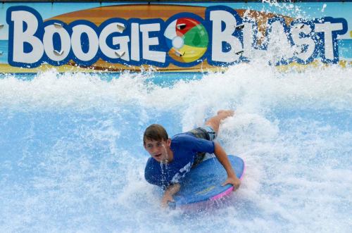 A young man rides a boogie board on a wave at a water park attraction called "Boogie Blast."