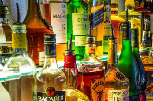 A variety of liquor bottles displayed on a shelf, including whiskey, rum, and liqueurs, with colorful labels.