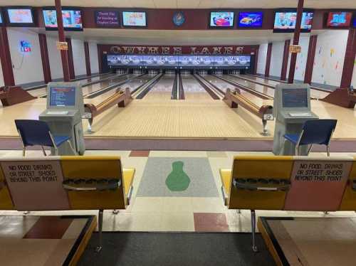 Interior of a bowling alley with lanes, seating, and signs prohibiting food and drinks beyond a certain point.