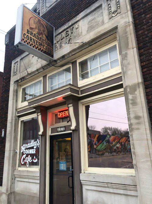 Exterior of Bradley's Corner Cafe, featuring a large "Open" sign and colorful mural visible through the windows.