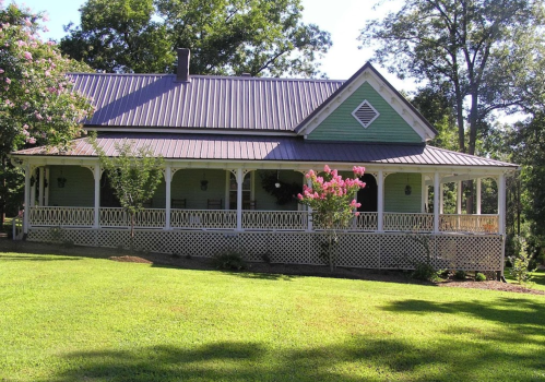A charming green house with a porch, surrounded by trees and a well-maintained lawn.