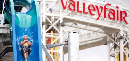 A child slides down a water slide at Valleyfair amusement park, with the park's sign visible in the background.
