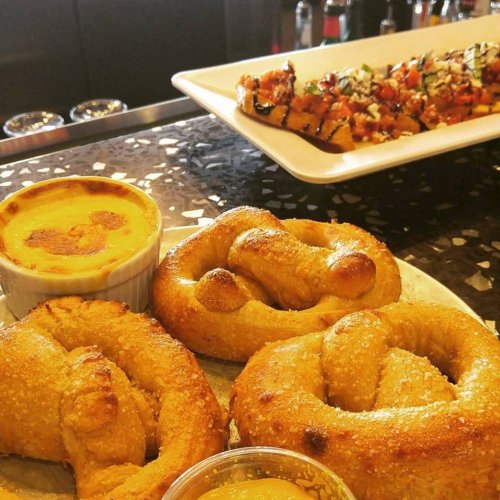 A plate of soft pretzels with mustard dip, alongside a dish of grilled skewers topped with vegetables.