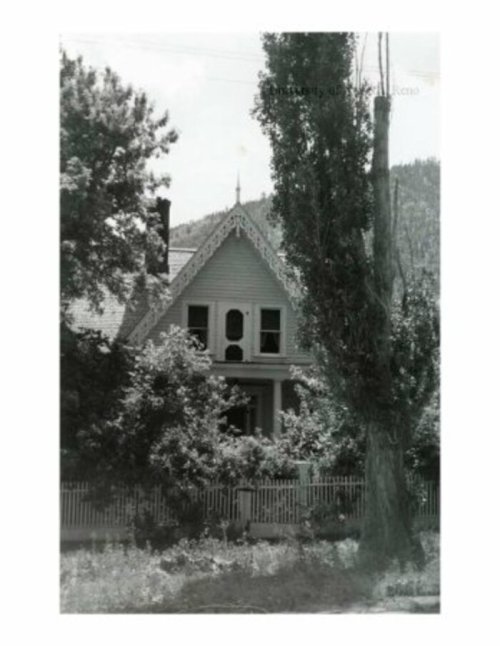 A vintage black-and-white photo of a large house surrounded by trees and a white picket fence.