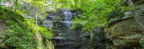 A serene waterfall cascading down rocky cliffs, surrounded by lush green trees and foliage.