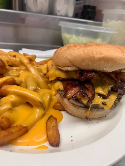 A close-up of a cheeseburger topped with bacon, served with a side of cheesy fries on a white plate.