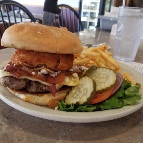 A large burger with bacon, cheese, and an onion ring, served with fries and pickles on a plate.