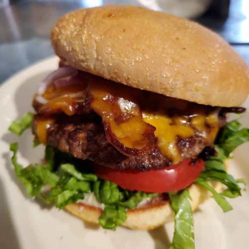 A juicy burger with melted cheddar, bacon, lettuce, and tomato, served on a sesame seed bun.