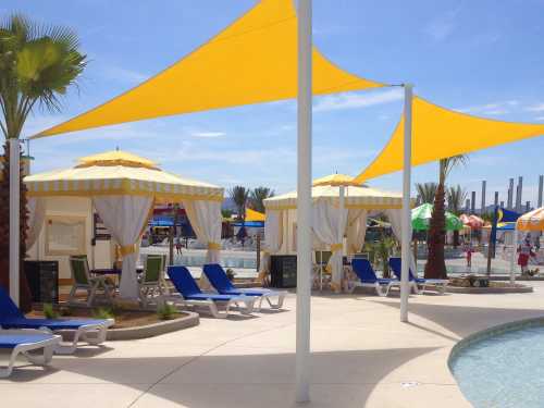 A sunny pool area with yellow cabanas, lounge chairs, and colorful umbrellas, surrounded by palm trees.