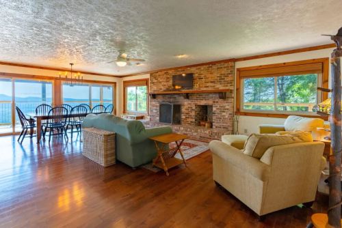 Cozy living room with a fireplace, large windows, and a dining area overlooking a scenic view. Warm wood accents throughout.