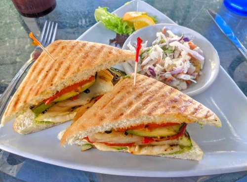 A toasted sandwich filled with grilled vegetables, served with a side of coleslaw and a lemon wedge on a plate.