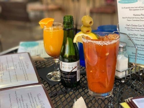 Two cocktails on a table: a mimosa with an orange slice and a Bloody Mary garnished with olives and a lemon wedge.