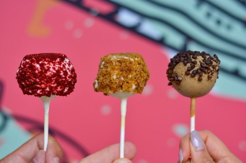 Three cake pops on sticks: red velvet, caramel, and chocolate chip, against a colorful background.