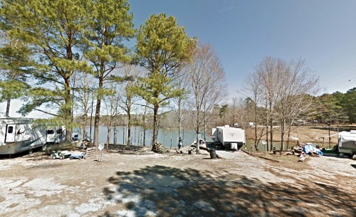 A serene lakeside scene with RVs and tall trees, reflecting a calm atmosphere on a sunny day.