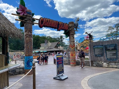 Entrance to Castaway Island amusement park, featuring tiki statues and a vibrant atmosphere with visitors enjoying the day.