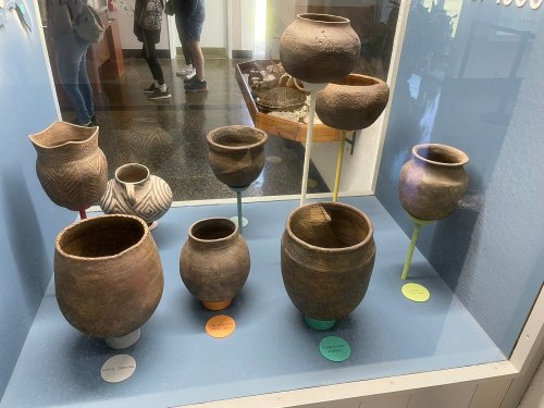 A display case featuring various ancient pottery pieces in different shapes and sizes, with colorful labels underneath.
