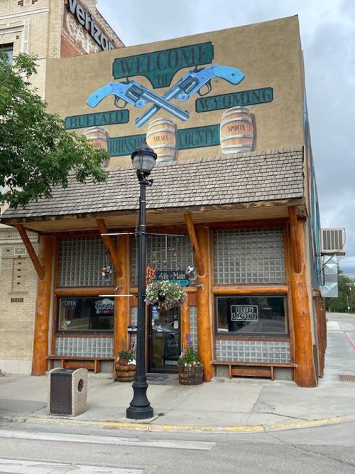 Mural reading "Welcome to Buffalo, Wyoming" on a building with wooden accents and a street lamp in front.
