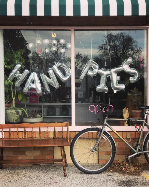 A storefront window displays "HAND PIES" in silver balloons, with a bicycle parked outside and greenery visible inside.