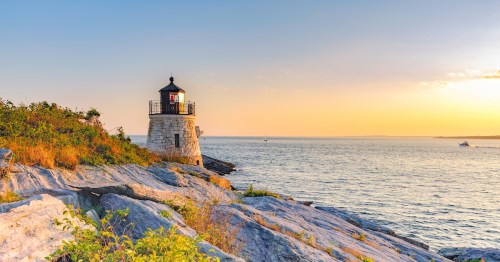 The iconic Castle Hill Lighthouse perched on rocky cliffs at sunset in Newport, Rhode Island.