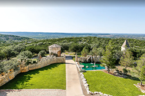 Scenic view of a landscaped area with stone walls, a pool, and rolling hills in the background under a clear blue sky.