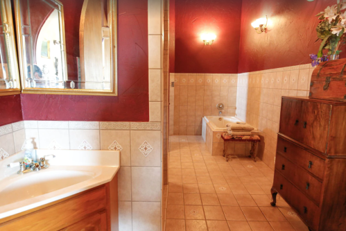 A spacious bathroom featuring a sink, bathtub, and wooden furniture against a red wall with decorative lighting.