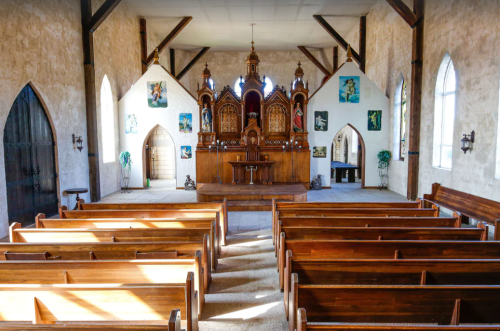 Interior of a church featuring wooden pews, an ornate altar, and decorative wall art. Bright and spacious atmosphere.